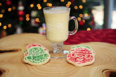 CLOSE UP VIEW. Christmas Cookies with Eggnog. Christmas Tree out of focus in the background with cookies and Eggnog for Santa. Cookies on a Tree Stump Cutting Board.