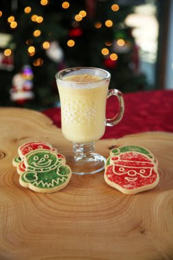 CLOSE UP VIEW. Christmas Cookies with Eggnog. Christmas Tree out of focus in the background with cookies and Eggnog for Santa. Cookies on a Tree Stump Cutting Board.