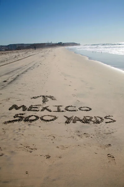 Words in sand. Mexico 500 yards with Arrow pointing towards Mexico written in the sand at the border between Mexico and the United States of America. Directional Signage.