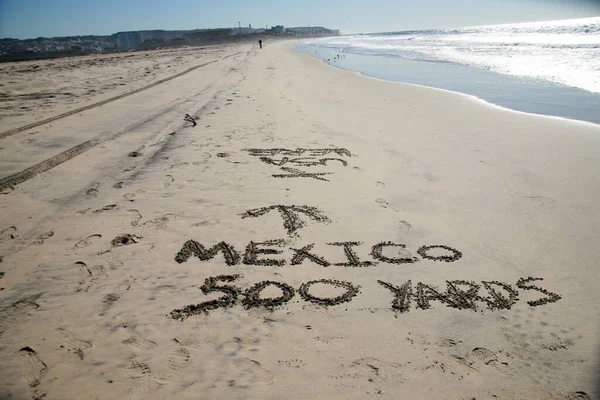 Words in sand. Mexico 500 yards with Arrow pointing towards Mexico written in the sand at the border between Mexico and the United States of America. Directional Signage.