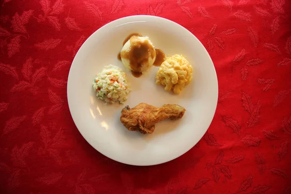 Chicken Dinner. Close Up View of a Chicken Dinner. White plate. Red Table Cloth. Chicken Leg. Biscuit. Coleslaw. Mashed Potatoes and Gravy. Macaroni and Cheese. A Meal fit for a King.