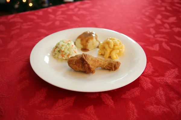 Chicken Dinner. Close Up View of a Chicken Dinner. White plate. Red Table Cloth. Chicken Leg. Biscuit. Coleslaw. Mashed Potatoes and Gravy. Macaroni and Cheese. A Meal fit for a King.