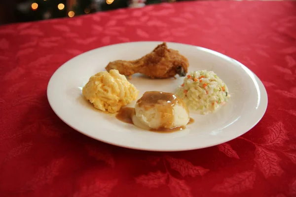 Chicken Dinner. Close Up View of a Chicken Dinner. White plate. Red Table Cloth. Chicken Leg. Biscuit. Coleslaw. Mashed Potatoes and Gravy. Macaroni and Cheese. A Meal fit for a King.