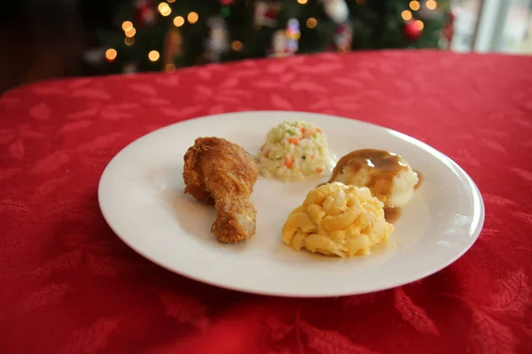 Chicken Dinner. Close Up View of a Chicken Dinner. White plate. Red Table Cloth. Chicken Leg. Biscuit. Coleslaw. Mashed Potatoes and Gravy. Macaroni and Cheese. A Meal fit for a King.