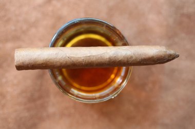 Küba purosu. Elle sarılmış Küba purosu. Deri bir masanın üstünde bir bardak viski. Mesaj için yer var. Tek malt viski, kristal bardakta viski ve deri üstünde Küba purosu.. 