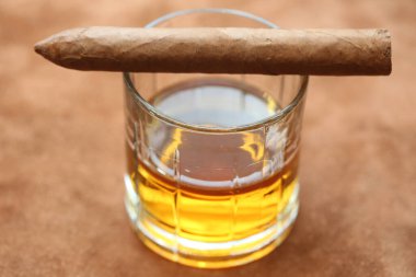 Küba purosu. Elle sarılmış Küba purosu. Deri bir masanın üstünde bir bardak viski. Mesaj için yer var. Tek malt viski, kristal bardakta viski ve deri üstünde Küba purosu.. 