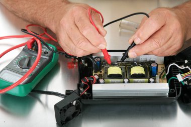 Elektronik Tamir Dükkanı. Bir insan elektrik sayacını elektrik devrelerini, arızaları ve şortları kontrol etmek için kullanır. Tezgahında elektrikli teçhizat test eden bir teknisyenin elleri. Çoklu sayacı olan bir teknisyen elleri. 