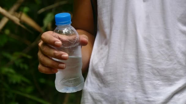 Молодий чоловік п'є з пляшки води в тропічному дощовому лісі — стокове відео