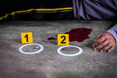 Adli tıp müfettişi olay yerindeki bir silahın fişeklerini vurguluyor.