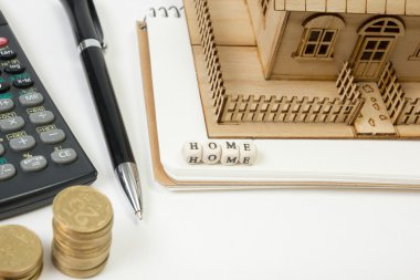 Konut satın alma ve sigorta kavramı. Ofis resepsiyon masası malzemeleri en iyi manzaralı. Hesap makinesi. altın sikke, kalem, not defteri, yeşil model evi, ahşap blok kelime