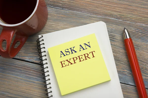 Ask an expert. Notepad with message, red pencil and coffee cup. Office supplies on desk table top view. — Stock Photo, Image