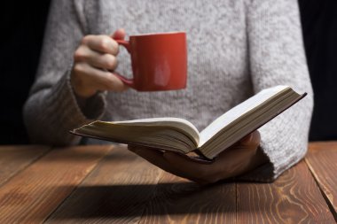 Bir kitap okuma ve fincan çay ya da kahve tutan genç kadın. Tonlu görüntü