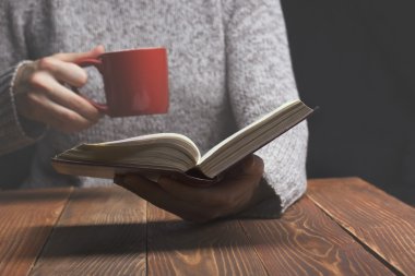Bir kitap okuma ve fincan çay ya da kahve tutan genç kadın. Tonlu görüntü