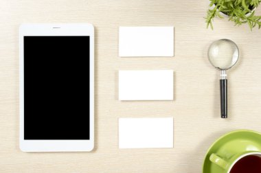 Kartvizit boş, akıllı telefon veya tablet pc, çiçek ve kahve fincanı, ofis masası masa üst görünümünde büyüteç. Kurumsal kırtasiye markalama maket