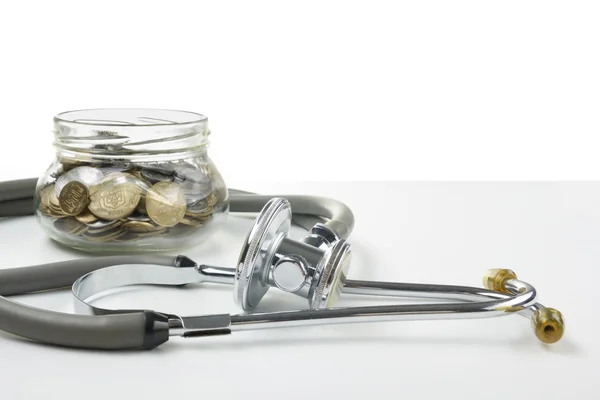 Glass bank with coins and medical stethoscope. Medical costs, financial concept.