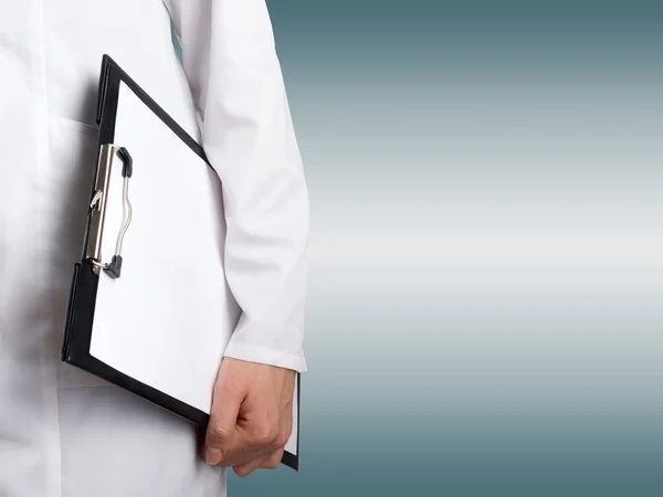 Die Hand einer Ärztin hält ein Klemmbrett mit leerem Blatt Papier auf verschwommenem Hintergrund. Gesundheitswesen und Medizin. Kopierraum. — Stockfoto