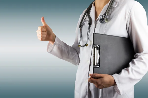 Female doctor's hand holding medical clipboard and stethoscope, giving thumbs up success sign gesture on blurred background. Concept of Healthcare And Medicine. Copy space. — Stock Photo, Image