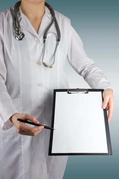 Mão de doutora feminina segurando uma caneta e prancheta com papel em branco (documento, relatório) e estetoscópio em fundo embaçado. Conceito de Saúde e Medicina. Espaço de cópia . — Fotografia de Stock