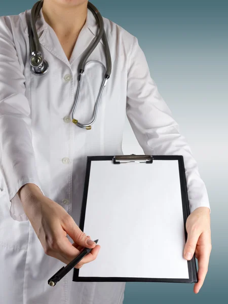 Mão de doutora feminina segurando uma caneta e prancheta com papel em branco (documento, relatório) e estetoscópio em fundo embaçado. Conceito de Saúde e Medicina. Espaço de cópia — Fotografia de Stock