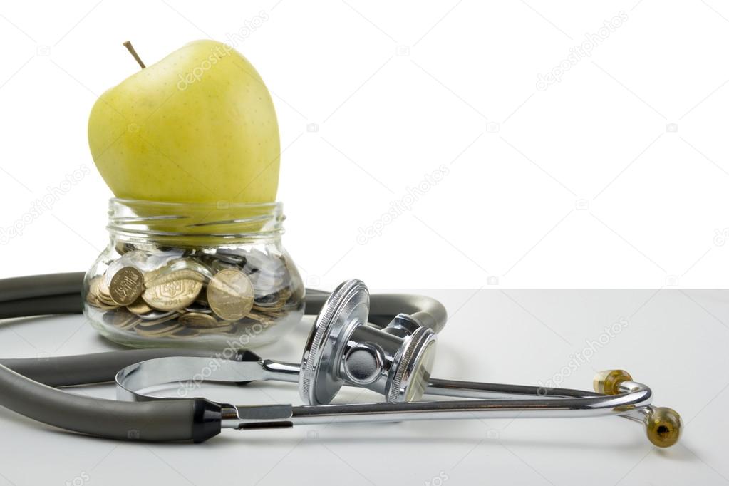 Glass bank with coins, green apple and medical stethoscope. Medical costs, financial concept.