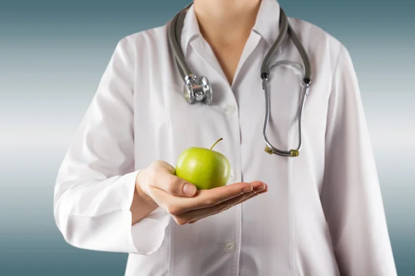 Mão de médica feminina segurando maçã verde. Fechar tiro no azul — Fotografia de Stock