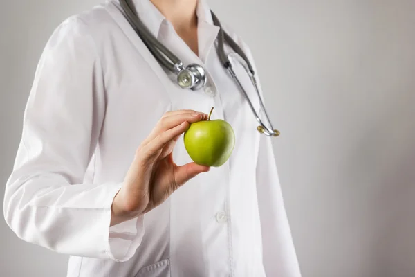 Mano de doctora sosteniendo manzana verde. Primer plano plano sobre gris —  Fotos de Stock