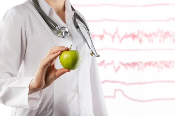Женщина-врач держит в руках зеленое яблоко. Крупный план на размытом медицинском фоне. Концепция здравоохранения и медицины. Копирование пространства — стоковое фото