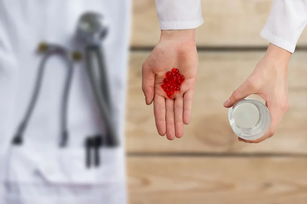 Doctor dando píldoras rojas y vaso de agua, las manos se cierran con el escritorio en el fondo, vista superior — Foto de Stock