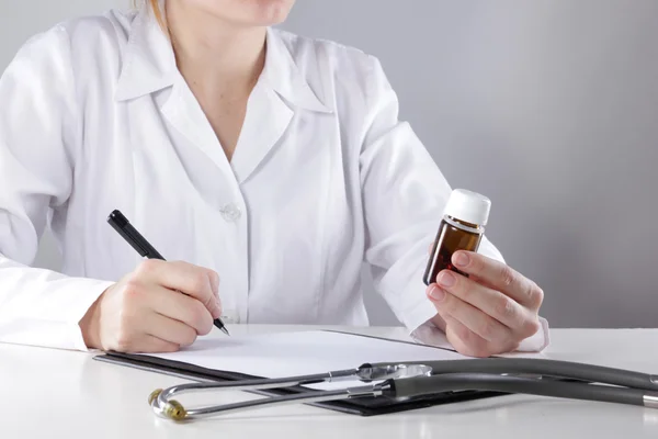 Young woman physician with stethoscope prescribing treatment to patient. Female doctor with pen writing recipe on clipboard in hospital. — Stock Photo, Image