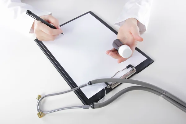 Young woman physician with stethoscope prescribing treatment to patient. Female doctor with pen writing recipe on clipboard in hospital. — Stock Photo, Image