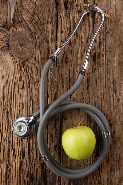 Alternatieve geneeskunde - stethoscoop en groene appel op houten tafelblad weergave. Medische achtergrond. Concept voor voeding, gezondheidszorg, voeding of medische verzekering — Stockfoto