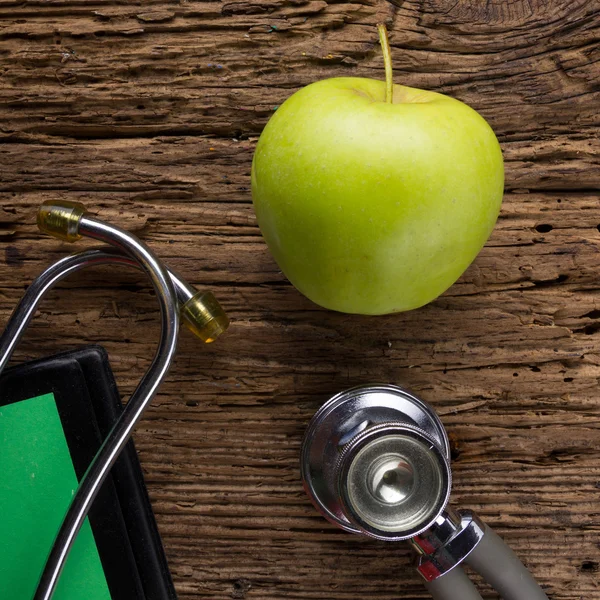 Alternatieve geneeskunde - stethoscoop, Klembord en groene appel op houten tafelblad weergave. Medische achtergrond. Concept voor voeding, gezondheidszorg, voeding of medische verzekering — Stockfoto