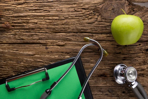 Medicina alternativa: estetoscopio, portapapeles y manzana verde en la vista superior de la mesa de madera. Formación médica. Concepto de dieta, salud, nutrición o seguro médico — Foto de Stock