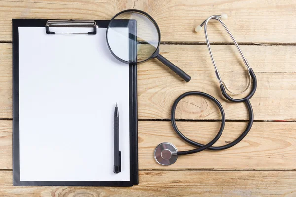 Munkahelyi orvosi. Tabletta, sztetoszkóp, fekete toll a fa asztal háttere. Szemközti nézet — Stock Fotó
