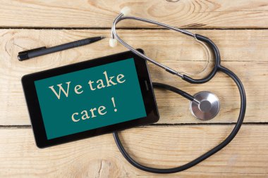 Kendine iyi bak! -Bir doktor işyeri. Tablet, sağlık stetoskop, ahşap Resepsiyon arka plan üzerinde siyah kalem. Üstten Görünüm