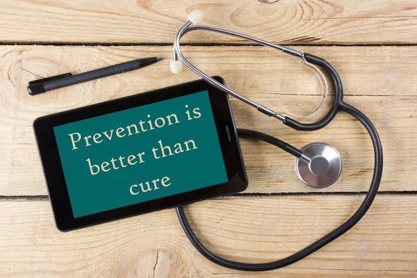 Prevention is better than cure - Workplace of a doctor. Tablet, medical stethoscope, black pen on wooden desk background. Top view