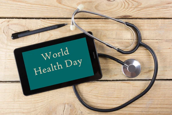 Ziua Mondială a Sănătății - locul de muncă al unui medic. Tabletă, stetoscop medical, stilou negru pe fundalul biroului din lemn. Privire de sus — Fotografie, imagine de stoc