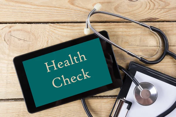 Health Check - Workplace of a doctor. Tablet, stethoscope, clipboard on wooden desk background. Top view — ストック写真