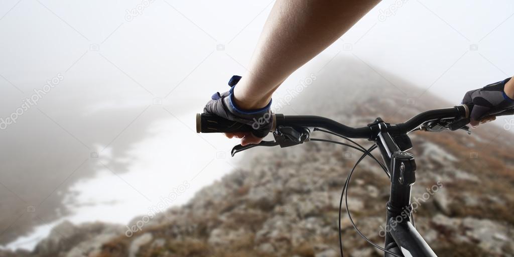 Hands in gloves holding handlebar of a bicycle. Mountain Bike cyclist riding single track. Healthy lifestyle active athlete doing sport