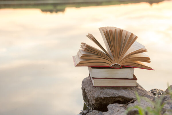 Stack of  book and Open hardback book on blurred nature landscape backdrop against sunset sky with back light. Copy space, back to school. Education background.