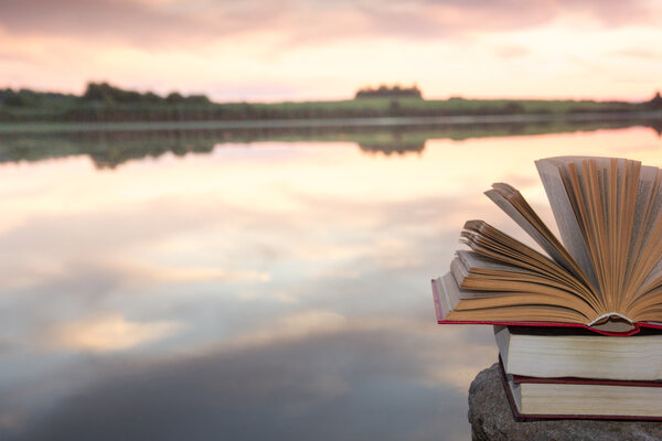 Stack of  book and Open hardback book on blurred nature landscape backdrop against sunset sky with back light. Copy space, back to school. Education background.