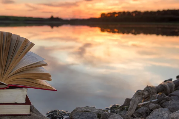 Stack of  book and Open hardback book on blurred nature landscape backdrop against sunset sky with back light. Copy space, back to school. Education background. — Stock Photo, Image