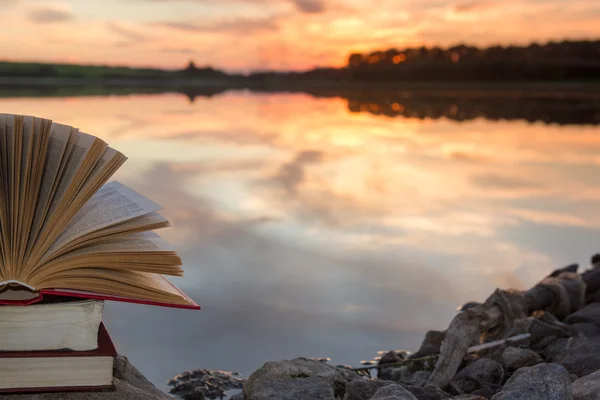 Stack of  book and Open hardback book on blurred nature landscape backdrop against sunset sky with back light. Copy space, back to school. Education background. — Stock Photo, Image