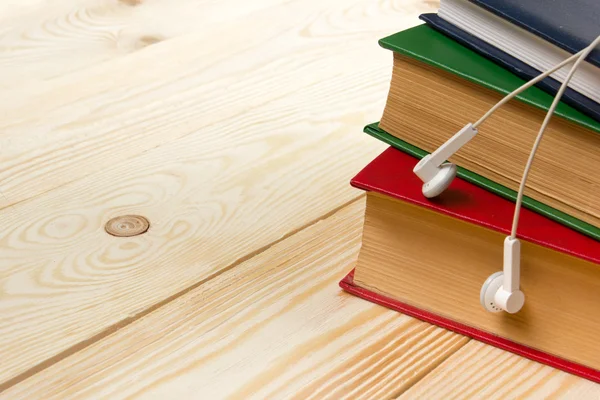 Ahşap masa ve kulaklık renkli kitap yığını. Audiobook kavramı