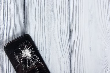 Modern cep telefonu Beyaz ahşap arka plan üzerinde kırık. Uzay kopyalayın. Üstten Görünüm