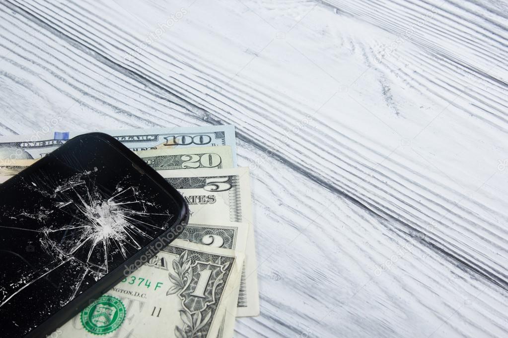 Modern broken mobile phone and money on white wooden background. Copy space. Top view
