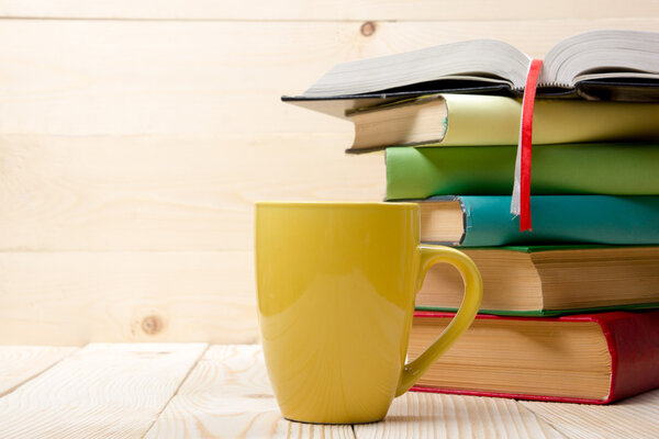 Stack of colorful books, open book and cup on wooden table. Back to school. Copy space