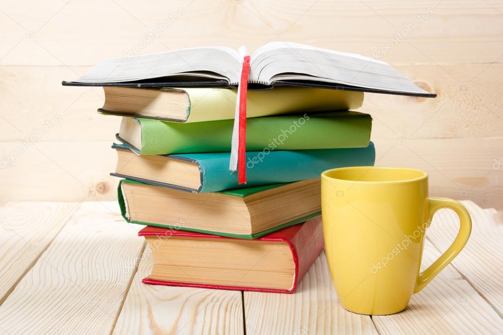 Stack of colorful books, open book and cup on wooden table. Back to school. Copy space