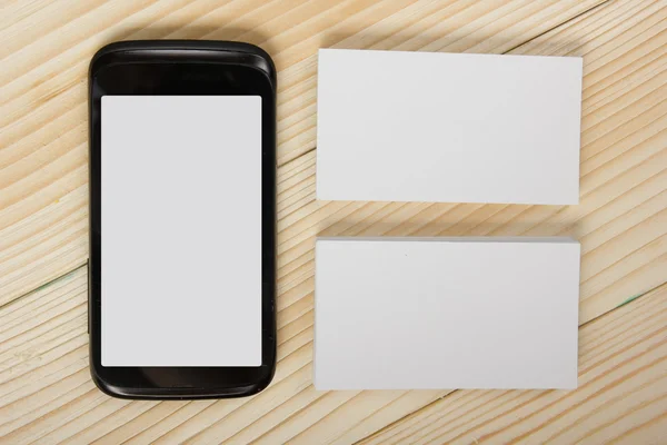 Cartões de visita brancos em branco e smartphone em fundo de madeira — Fotografia de Stock