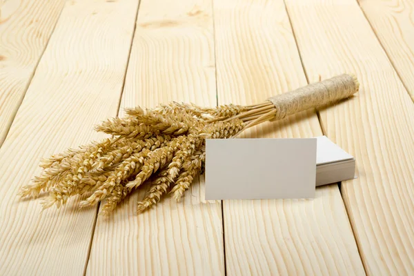 Orecchie di grano su tavolo di legno con biglietti da visita in bianco. Lenzuolo di grano su fondo di legno. Concetto di raccolta . — Foto Stock